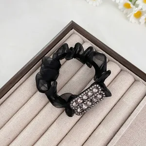 Gros plan sur l'échevelé chouchou en maille noire avec détail élégant de strass rectangulaire.