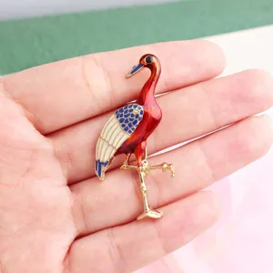 Gedetailleerd close-up van de emaille kraanvogel broche met heldere rode en blauwe kleuren.