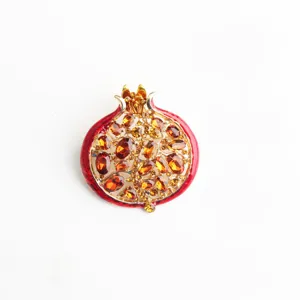 Primo piano dettagliato di una spilla melograno in smalto rosso con scintillanti strass ambra.