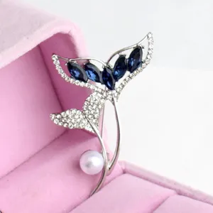 Detailed closeup of exquisite fish tail brooch with blue crystals and pearl in a pink box.