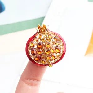 Dettaglio spilla melograno squisita, smalto rosso e strass ambra, elegante accessorio per cappotto.