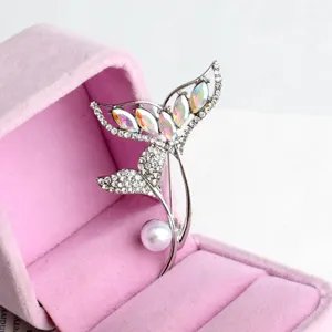 Detailed view of a stunning rhinestone and pearl fish tail brooch in a pink velvet box.