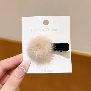 Close-up detail of the cute fluffy faux fur ball hair clip on a display card, soft plush texture.