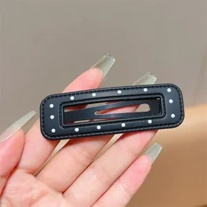 Detail shot of black leather hair clip with white polka dots, showing texture and BB clip design.