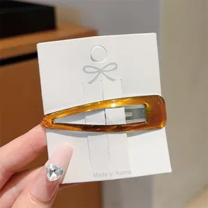 Close up detail of amber tortoiseshell oval snap hair clip on card, minimalist style.