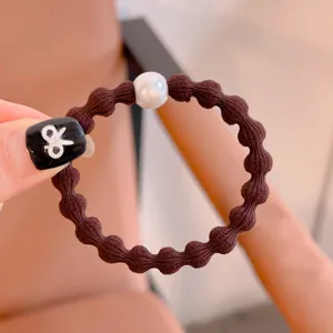 Detail view of brown elastic hair tie with white pearl charm, simple daily hair accessory.