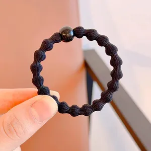 Detail view of the black wavy elastic hair tie with small bead, simple daily hair accessory.