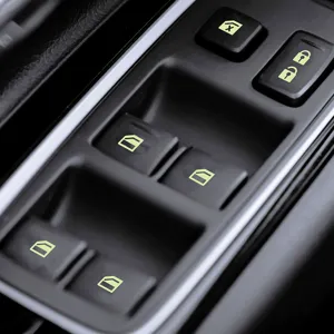 Detail view of car window switch luminous stickers, fluorescent buttons for night driving safety.