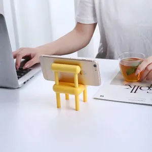 Detailed view of a cute yellow mini chair phone holder resting on a clean white desk setup.