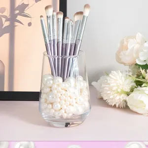 Set di pennelli da trucco con manici metallici viola in un bicchiere di perle bianche.