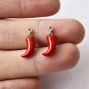 Detailopname van mini rode chili geëmailleerde hanger charms met gouden en zilveren ringen.