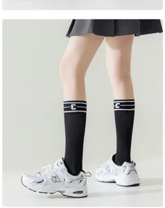 Detailed shot of black mid-calf socks with white stripes and letter C design worn by model.