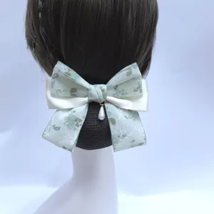Detail view of elegant green lace hair bow with pearl pendant, professional hairnet bun cover.