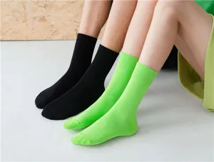 Nahaufnahme zeigt lebendige einfarbige Mittelsocken in Schwarz und Grün, ordentlich getragen.