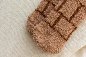 Gros plan détaillé de chaussettes de sommeil douces en polaire corail à carreaux marron.