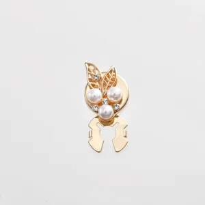 Close-up detail of golden metal clothing accessory featuring delicate pearl and rhinestone design.