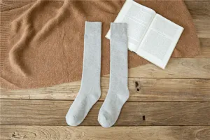 Detailed close-up view of cozy light grey knitted long tube socks on rustic wooden table.