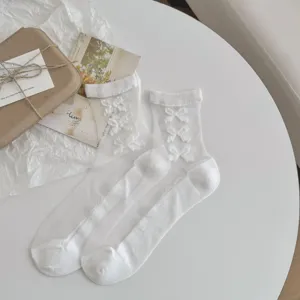 Détails de chaussettes transparentes blanches avec des nœuds sur une table blanche.
