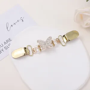 Close-up detail of the vintage rhinestone butterfly and pearl cardigan clip on white tray.
