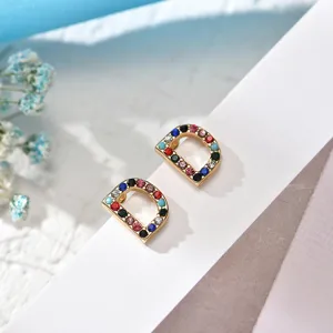 Close-up detail of stylish letter D stud earrings, colorful pavé rhinestones, chic copper jewelry.