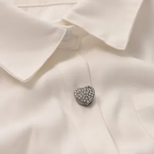 Gros plan d'un bouton cœur en cristal étincelant sur un chemisier blanc élégant et chic.