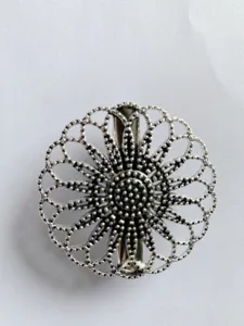 Close-up detail of vintage silver hollow carved flower brooch shawl clip ornament accessory.
