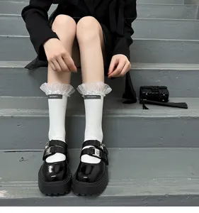 Detail shot of white mid-calf socks with sheer lace ruffle cuffs and black label on grey steps.