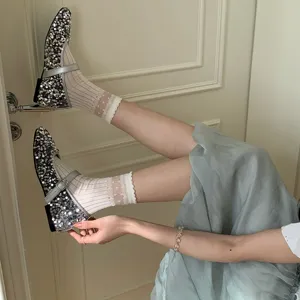 Detail shot of sparkling sequin Mary Jane shoes and sheer dotted lace socks in a cozy room.