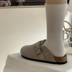 Calzini medi bianchi a coste da donna abbinati a scarpe mules casual in pelle scamosciata.