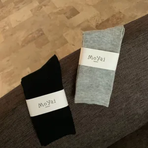 Dettagli di calze a tubo medio a coste in cotone nero e grigio con carta di imballaggio.