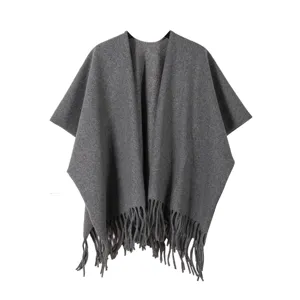 Gros plan sur les détails du poncho en tricot gris foncé à franges, texture chaude douce.