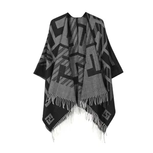 Primo piano dettagliato di mantella in maglia nera e grigia con motivo geometrico e frange.