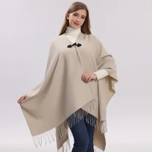 Détail d'une élégante cape en tricot beige avec fermeture à bascule noire et franges délicates.