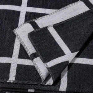 Close-up detail of black and white plaid scarf, showing neat overlocked edge and soft texture.