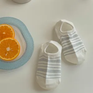 Close-up detail of white low-cut short socks with grey stripes on clean white table.