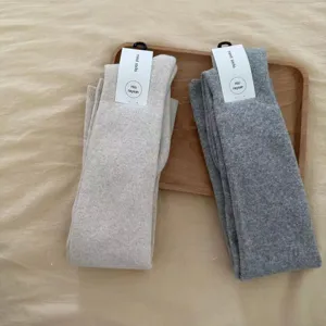 Closeup detail shot of thick over-the-knee loop knit socks in beige and grey on wooden tray.