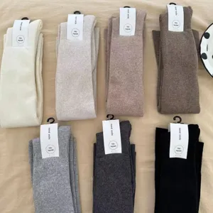 Detail view of thick knitted over-the-knee socks in multiple neutral colors, flat lay.