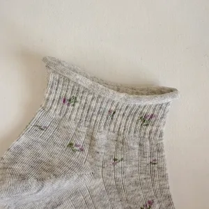 Detalle en primer plano de calcetines de punto gris para mujer con bordado floral y ribete.