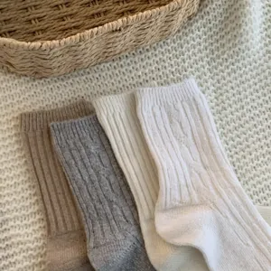 Close-up detail of cozy cable-knit winter socks in neutral colors on woven texture.