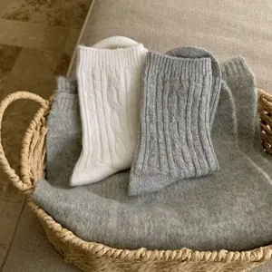 Close-up detail of cozy cable knit winter socks in white and grey displayed inside a woven basket.