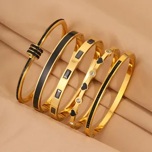 Detailansicht von fünf stilvollen goldenen Titanstahl-Armbändern mit schwarzen Einlagen.