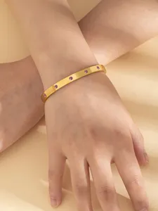Primo piano dettagliato di un elegante bracciale rigido in acciaio dorato con strass rosa.