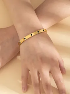 Primo piano di un elegante bracciale rigido in acciaio titanio dorato con pietre nere.