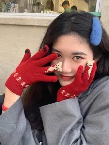 Close-up detail view of cute red knit winter gloves with cat pattern worn outside.