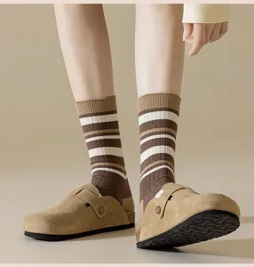 Detail shot of brown striped mid-tube socks paired with stylish suede clogs, cozy fall footwear.