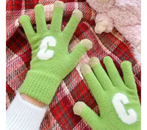 Nahaufnahme von grünen Strickhandschuhen mit weißem Buchstaben C und Metallic-Fingerspitzen.