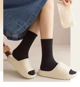 Detailed view of women's solid black mid-tube socks worn with casual beige slide sandals.