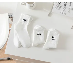 Detailed shot of white mid-tube socks with cute embroidered funny expressions on clean desk.