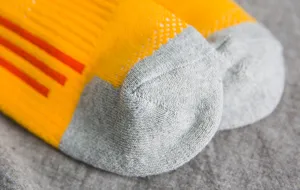 Gedetailleerde close-up van sportsokken met versterkte grijze hiel en geel gebreid materiaal.