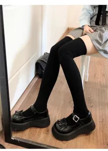 Primo piano di calze alte nere sopra il ginocchio con scarpe platform, maglia elastica.